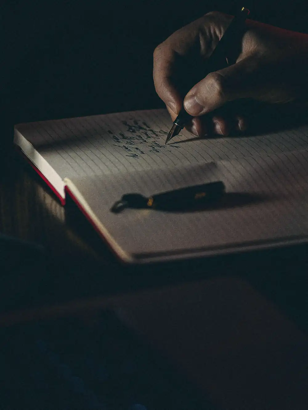 Late at night, a hand writing notes in a notebook on a dark desk